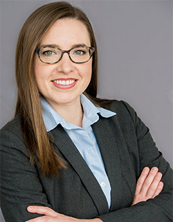 Professional-looking female with brown, long hair, wearing glasses and a suit.