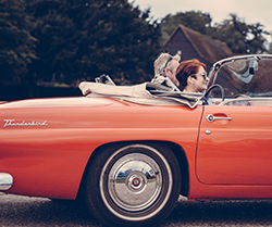 photo of older couple driving a red Ford Thunderbird
